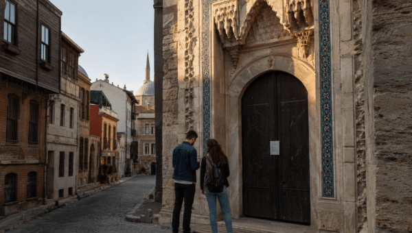 Closed Ottoman gateway in Istanbul with two travellers checking a phone, a dome and minaret behind