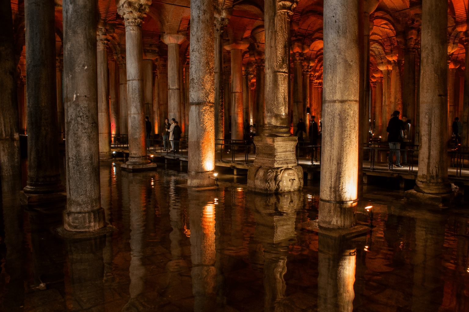 Columns rising from shallow reflective water in the Basilica Cistern with a Medusa head base beyond