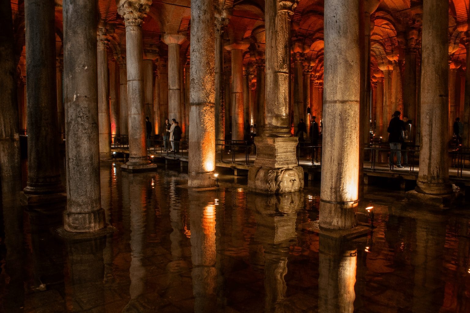 Columns rising from shallow reflective water in the Basilica Cistern with a Medusa head base beyond